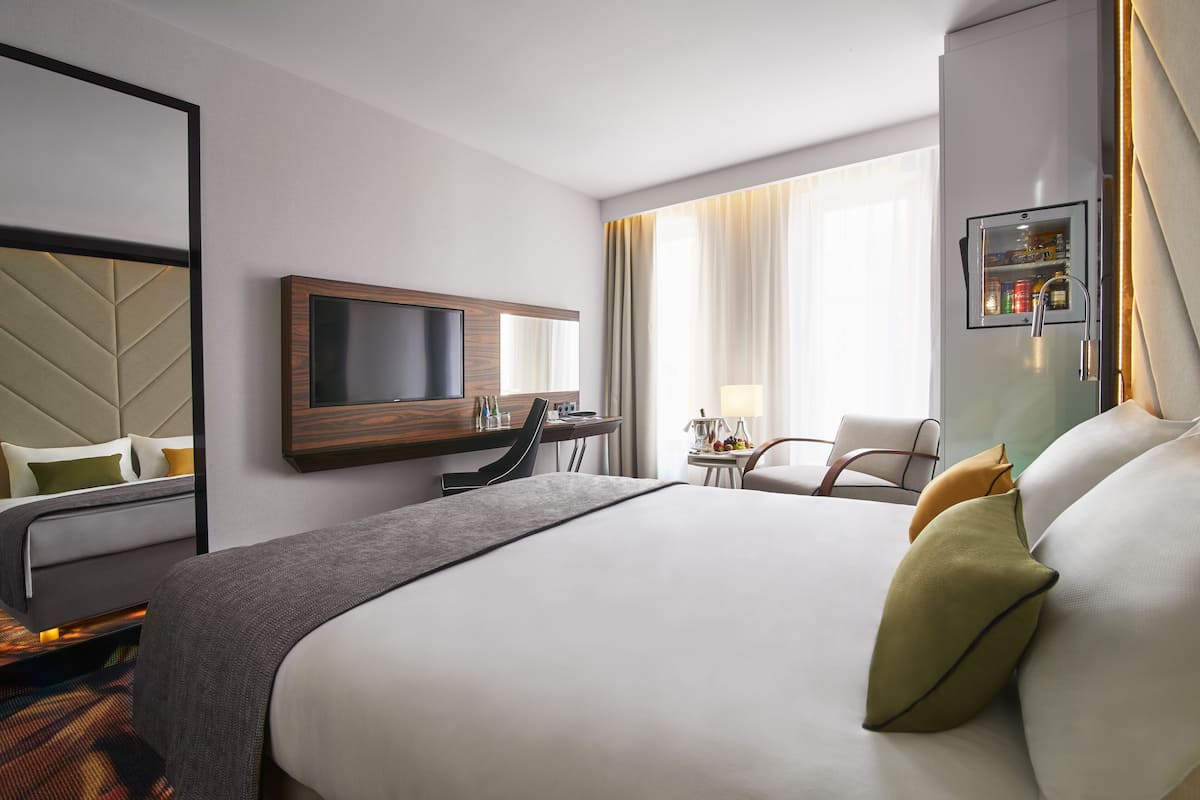 Habitación de hotel con cama, escritorio, televisor, silla y minibar.