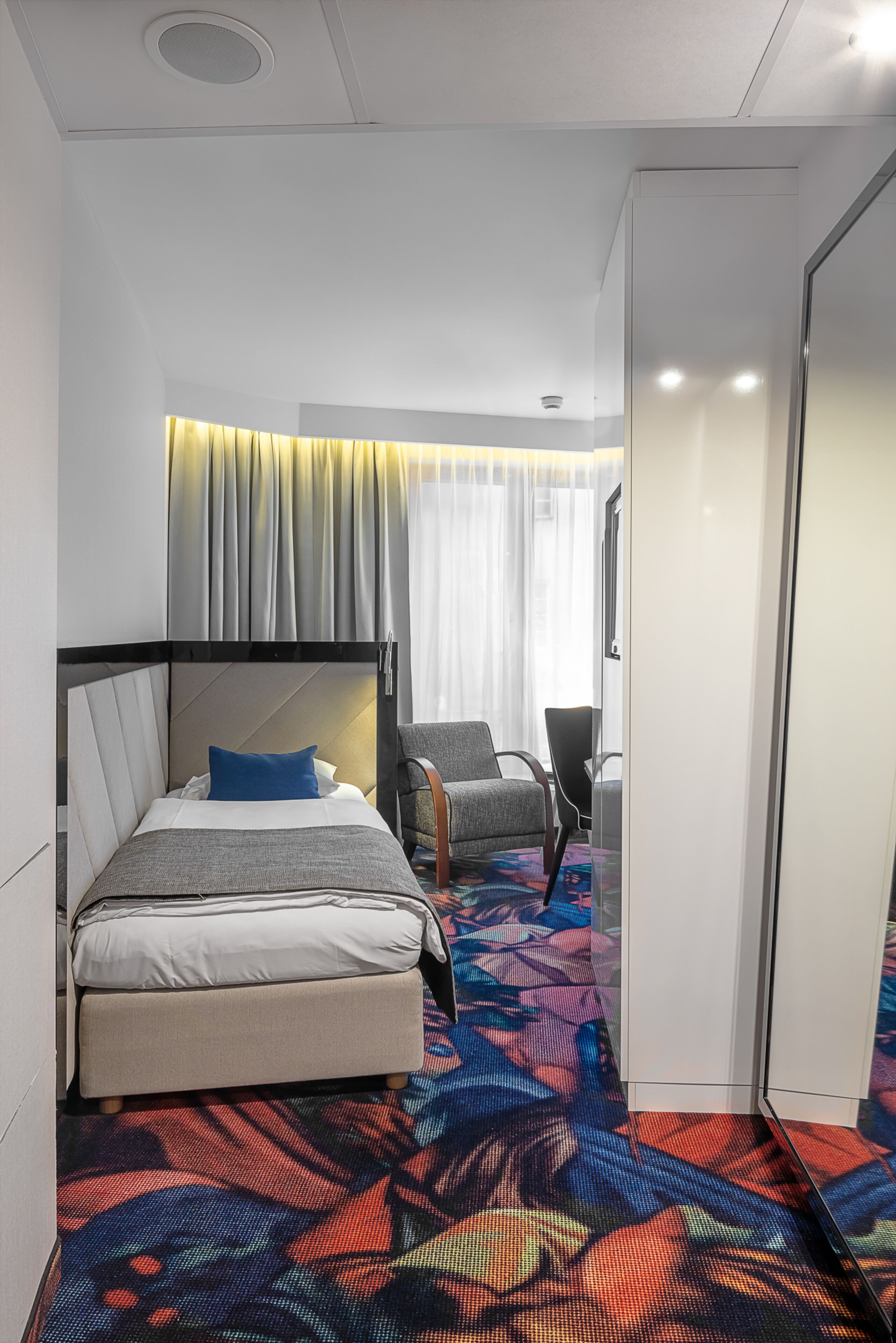 Habitación de hotel con cama, una silla, armario y alfombra estampada.