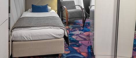 Habitación de hotel con cama, una silla, armario y alfombra estampada.