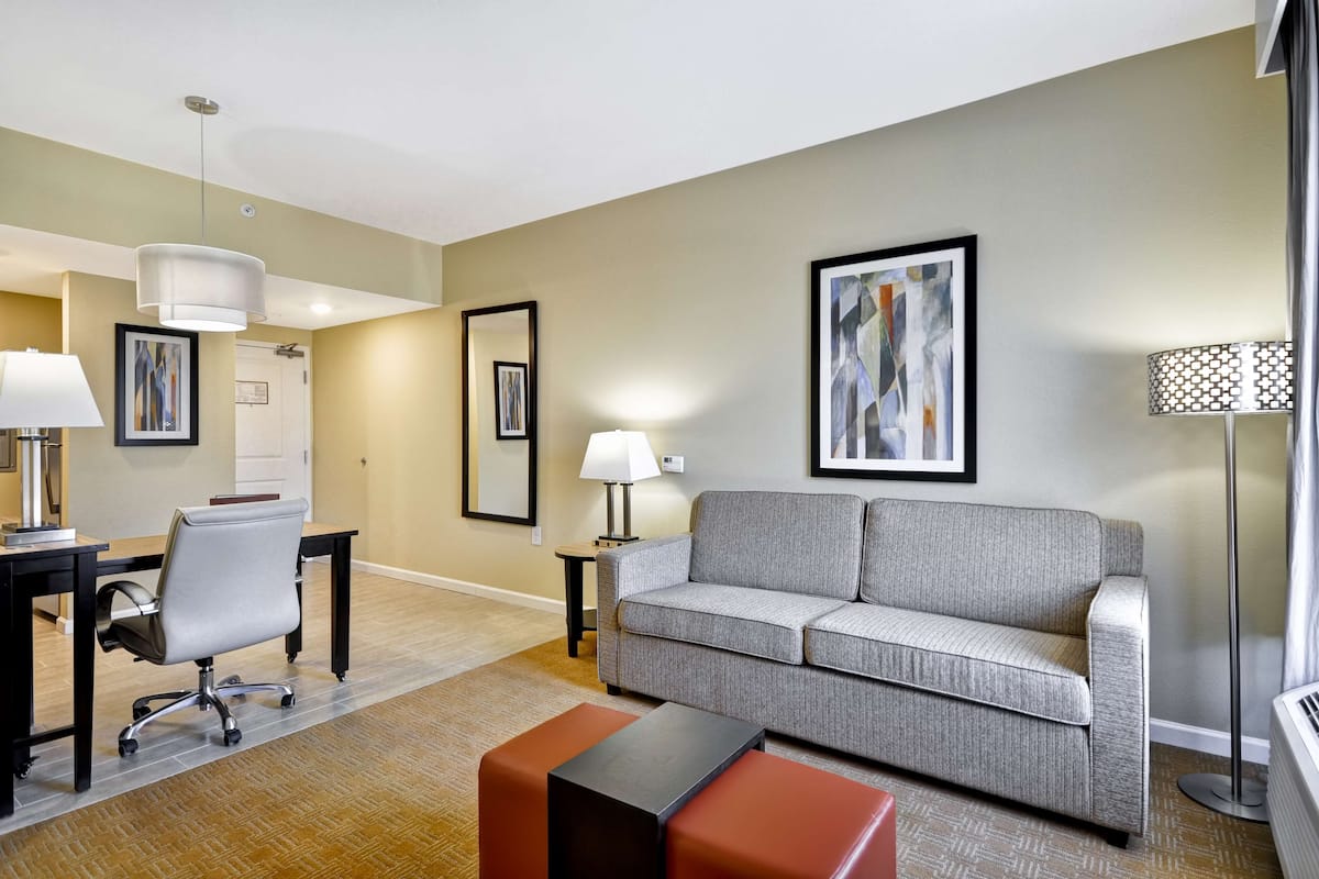 A modern living room with a grey sofa, a black office chair, a small table, and a floor lamp.