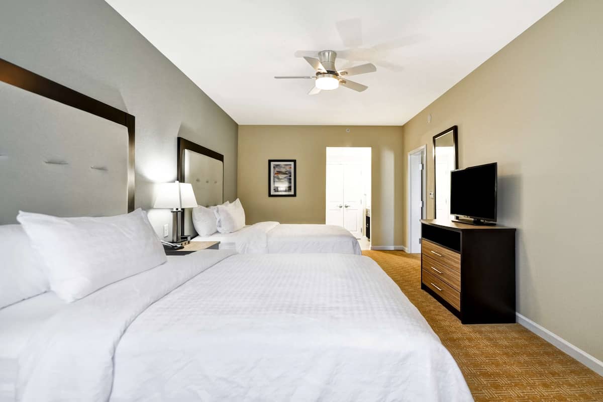 A hotel room with two beds, a ceiling fan, a television, and a dresser.