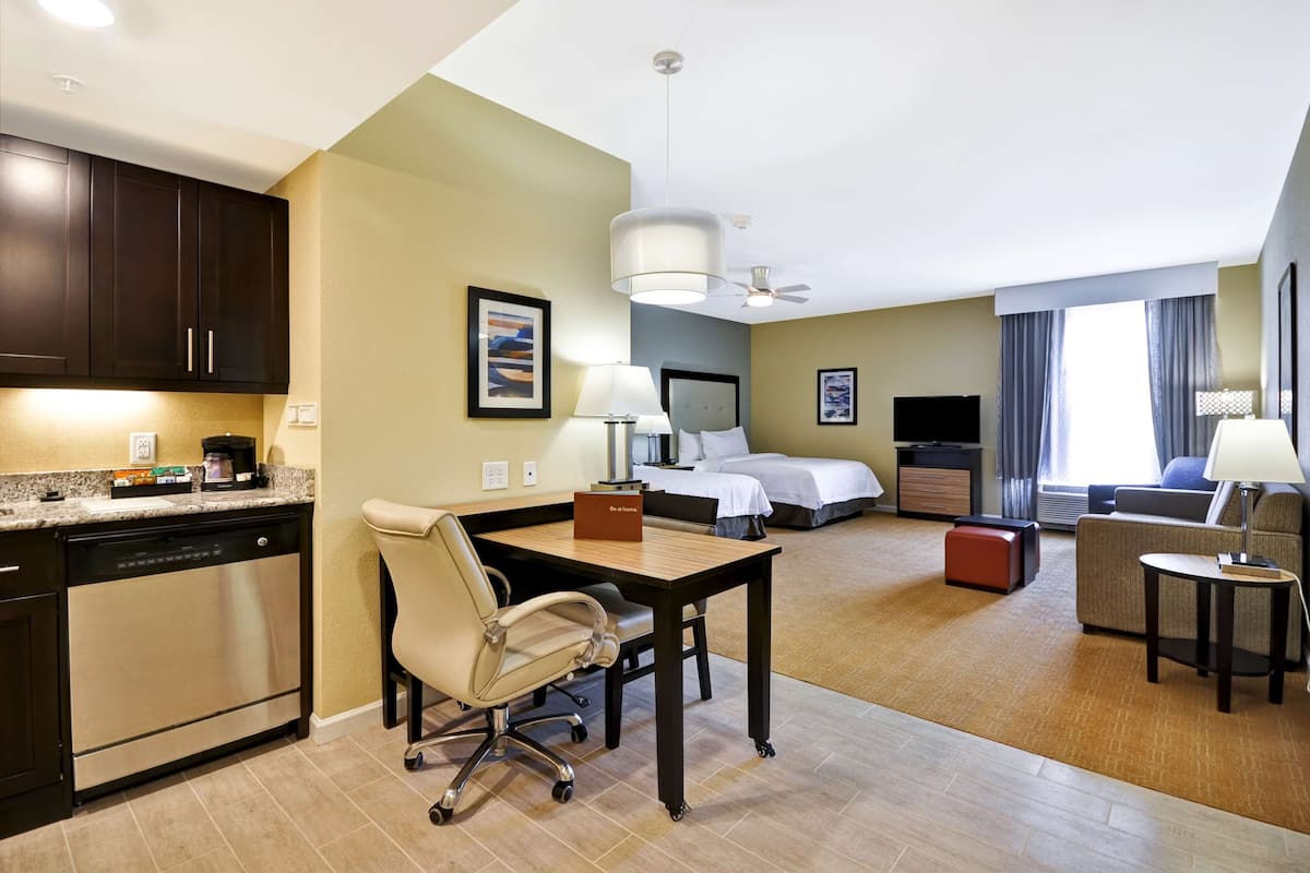 A hotel room with a kitchenette, a dining area, a bed, a sofa, and a TV.