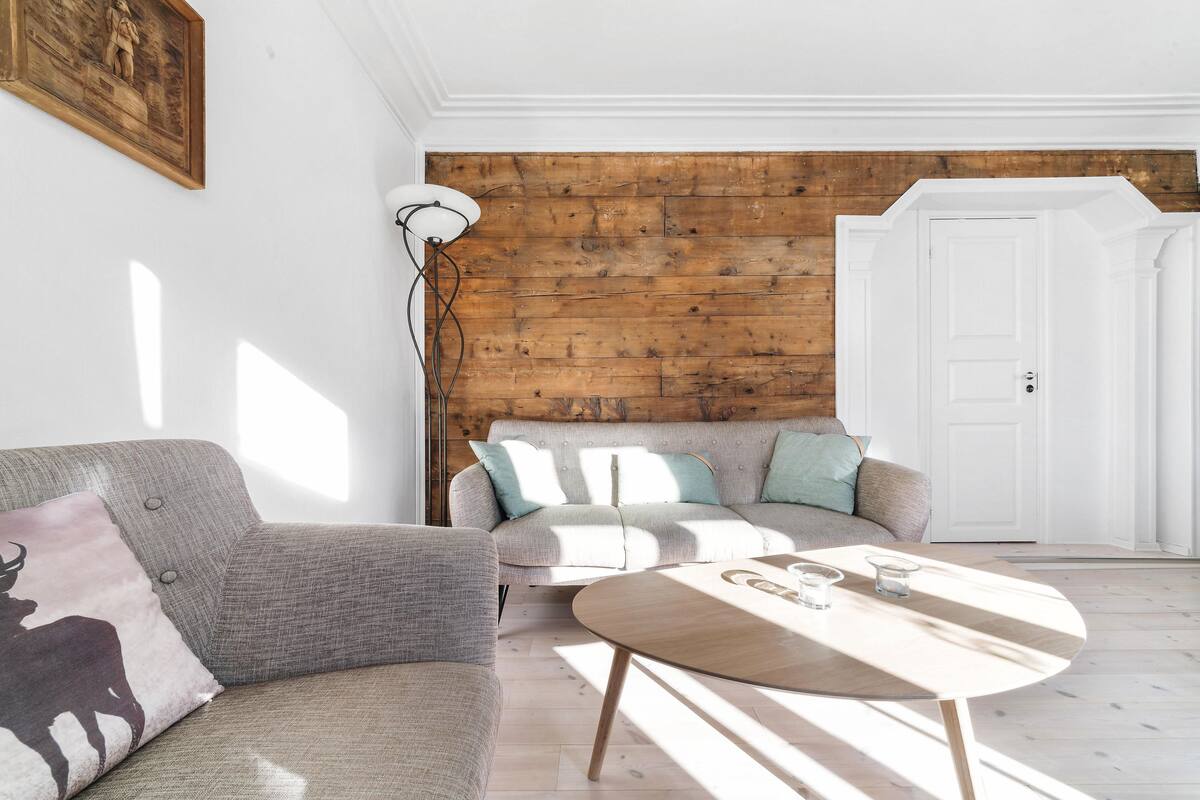 A living room with a grey sofa, a round wooden coffee table, and a white lamp.