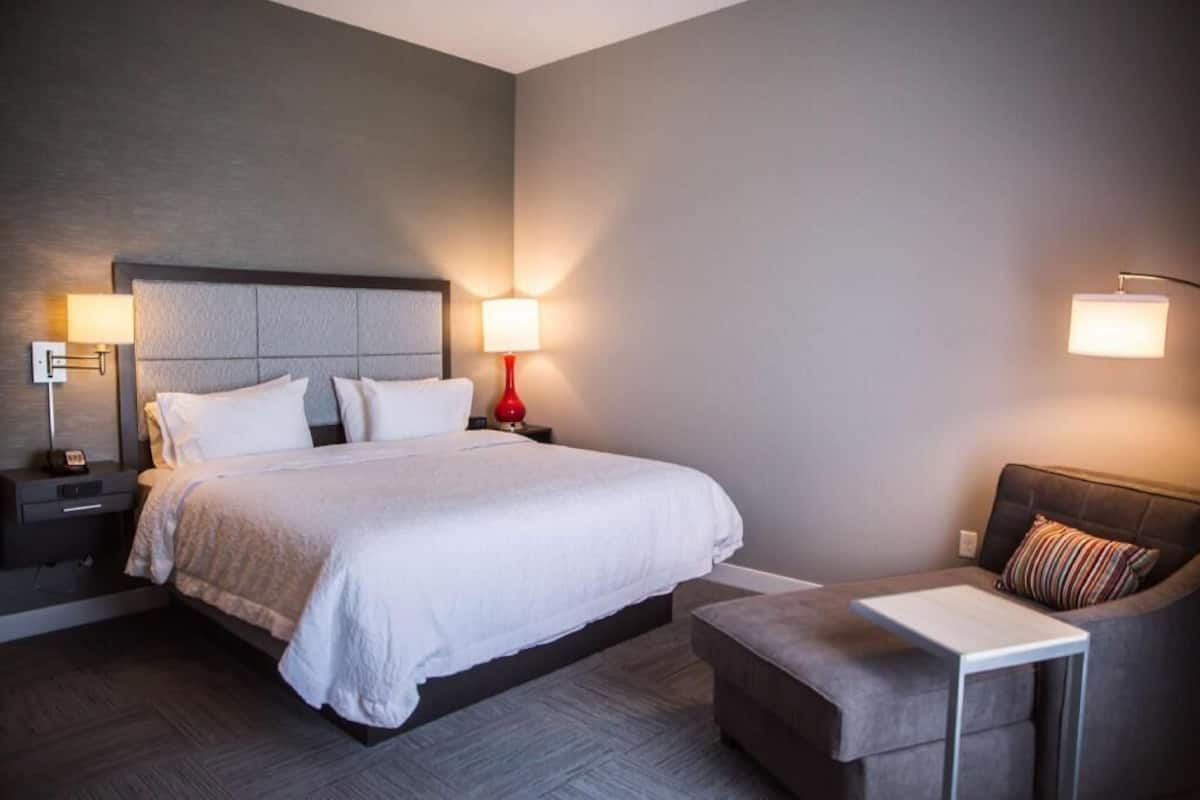 Una habitación de hotel con una cama grande, mesitas de noche, una silla y una pequeña mesa.