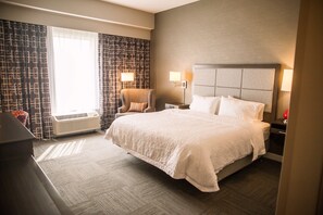 A hotel room with a large bed, a chair, a nightstand, and a window with curtains.
