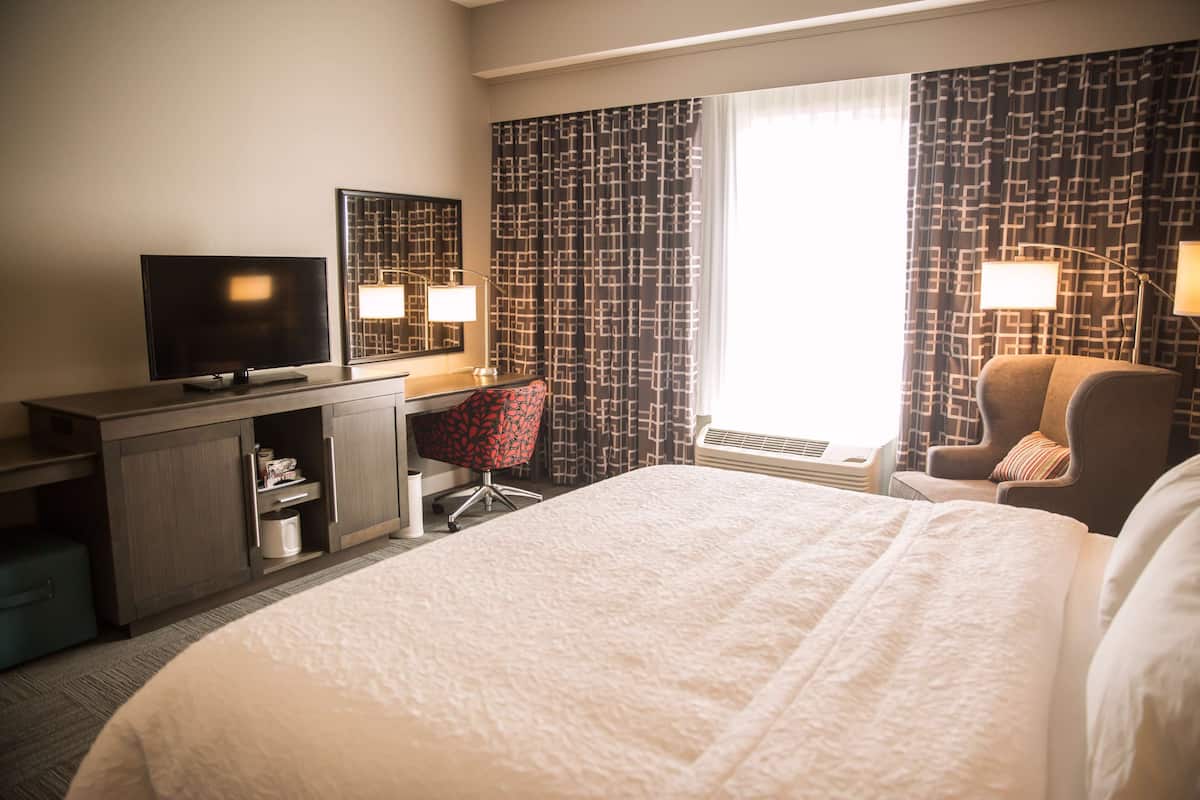 Habitación de hotel con cama, escritorio con televisor de pantalla plana, silla, lámpara y ventana con cortinas estampadas.