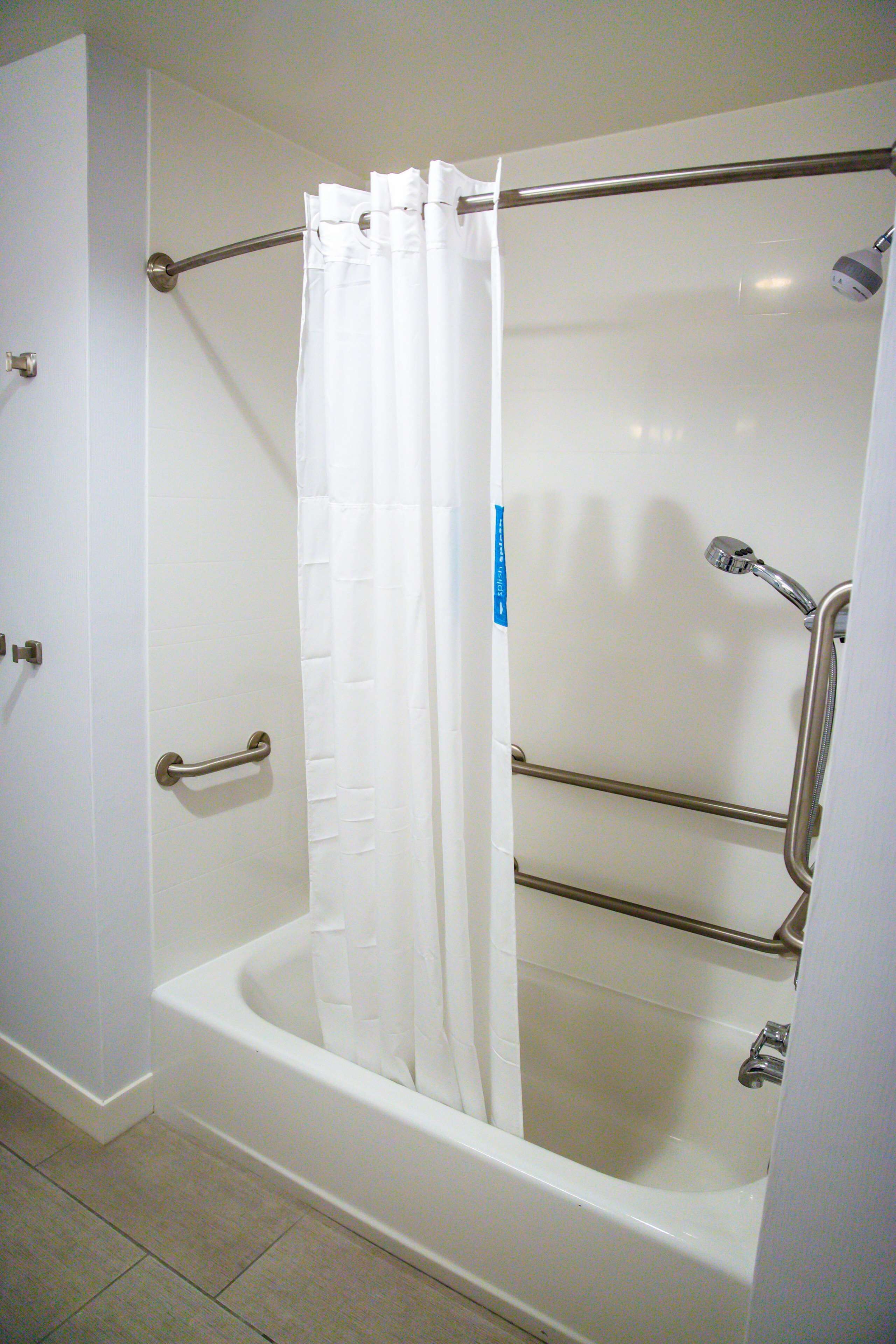 A walk-in bathtub with a shower curtain, grab bars, and a handheld showerhead.