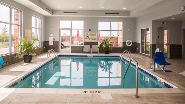 An indoor swimming pool with clear safety signs, a lifeguard chair, and a view of the outside through large windows. - Hampton Inn Pontiac (Pontiac)