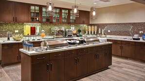A modern kitchen with wooden cabinets, a central island with a grill, and a variety of food dispensers.