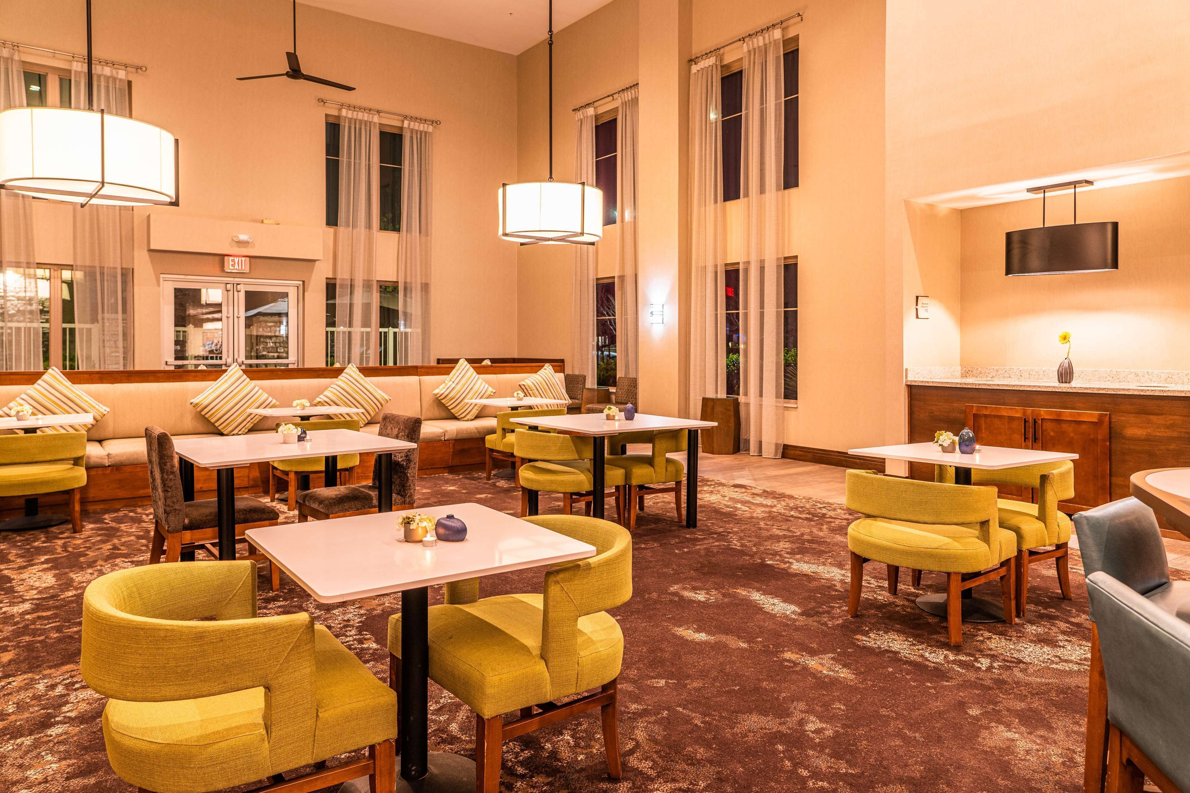 A hotel lobby with yellow chairs, white tables, and a large mirror.