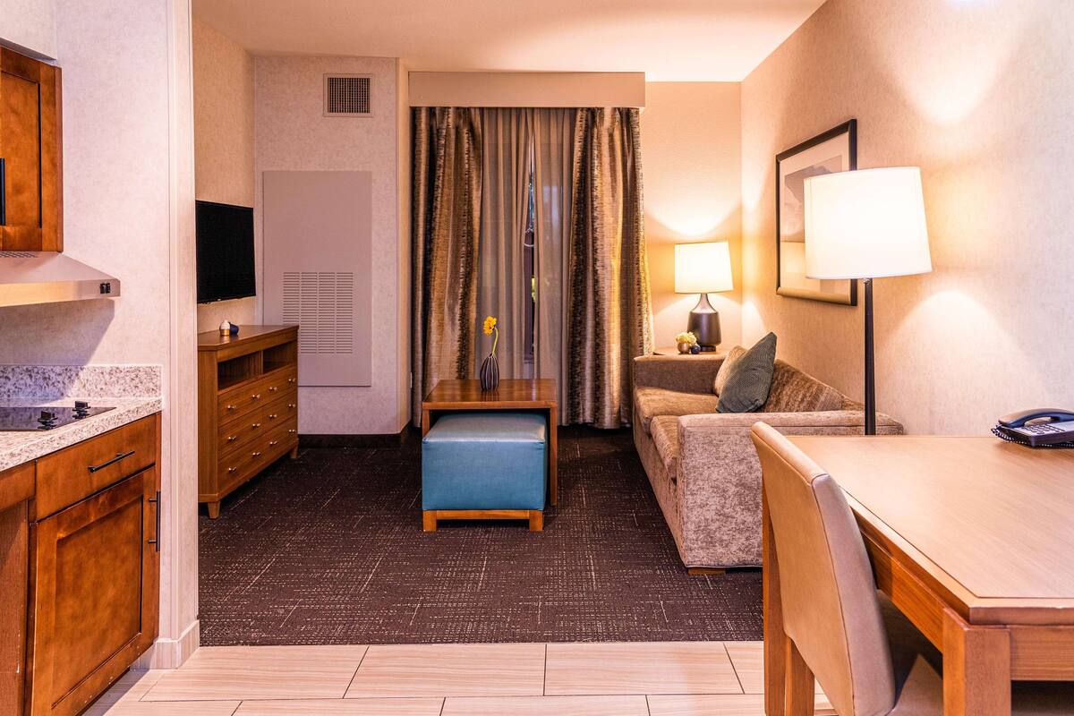 Een compacte hotelkamer met een kitchenette, een bank, een eettafel en een televisie.