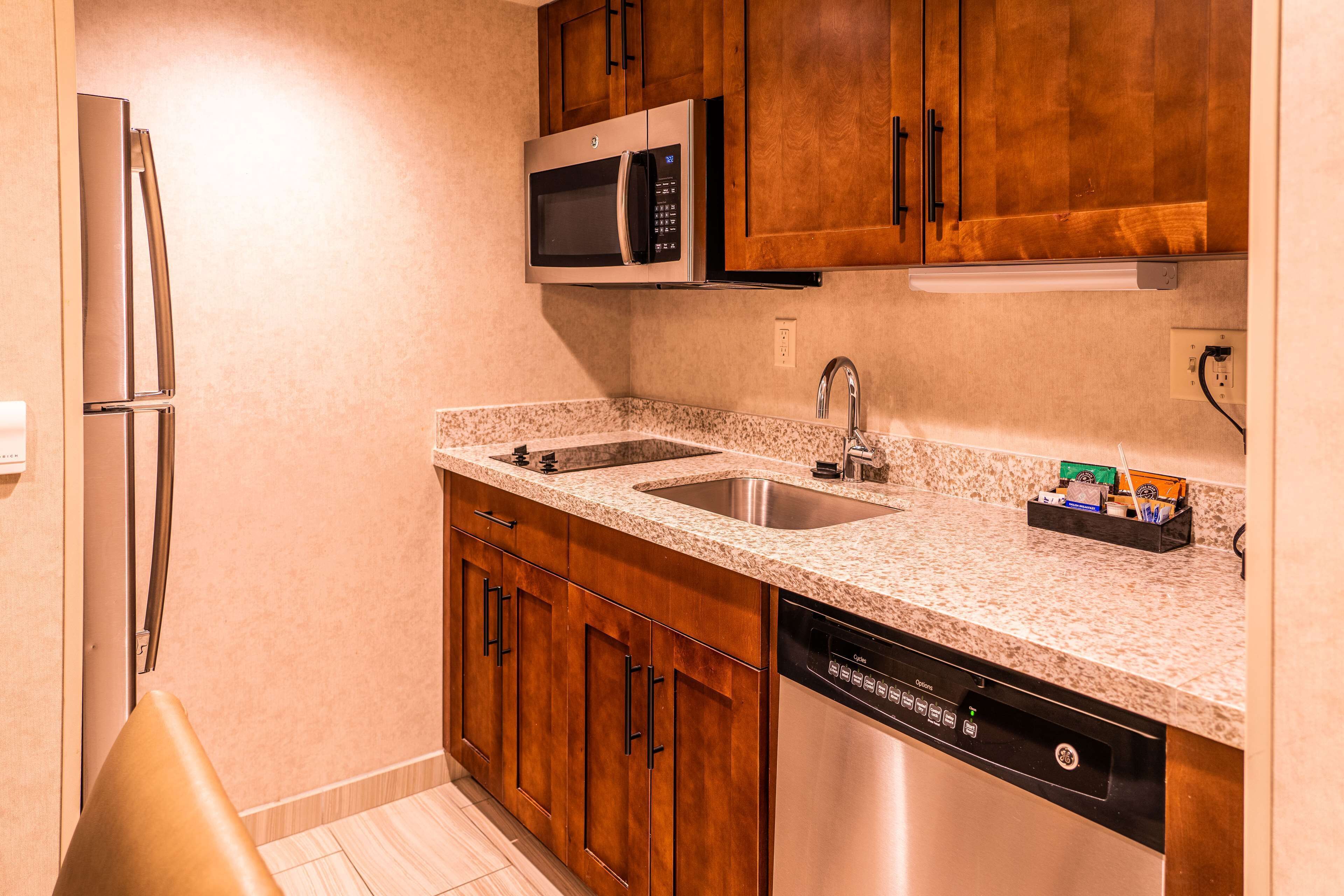 A compact kitchen with wooden cabinets, stainless steel appliances, a double sink, and a dishwasher.