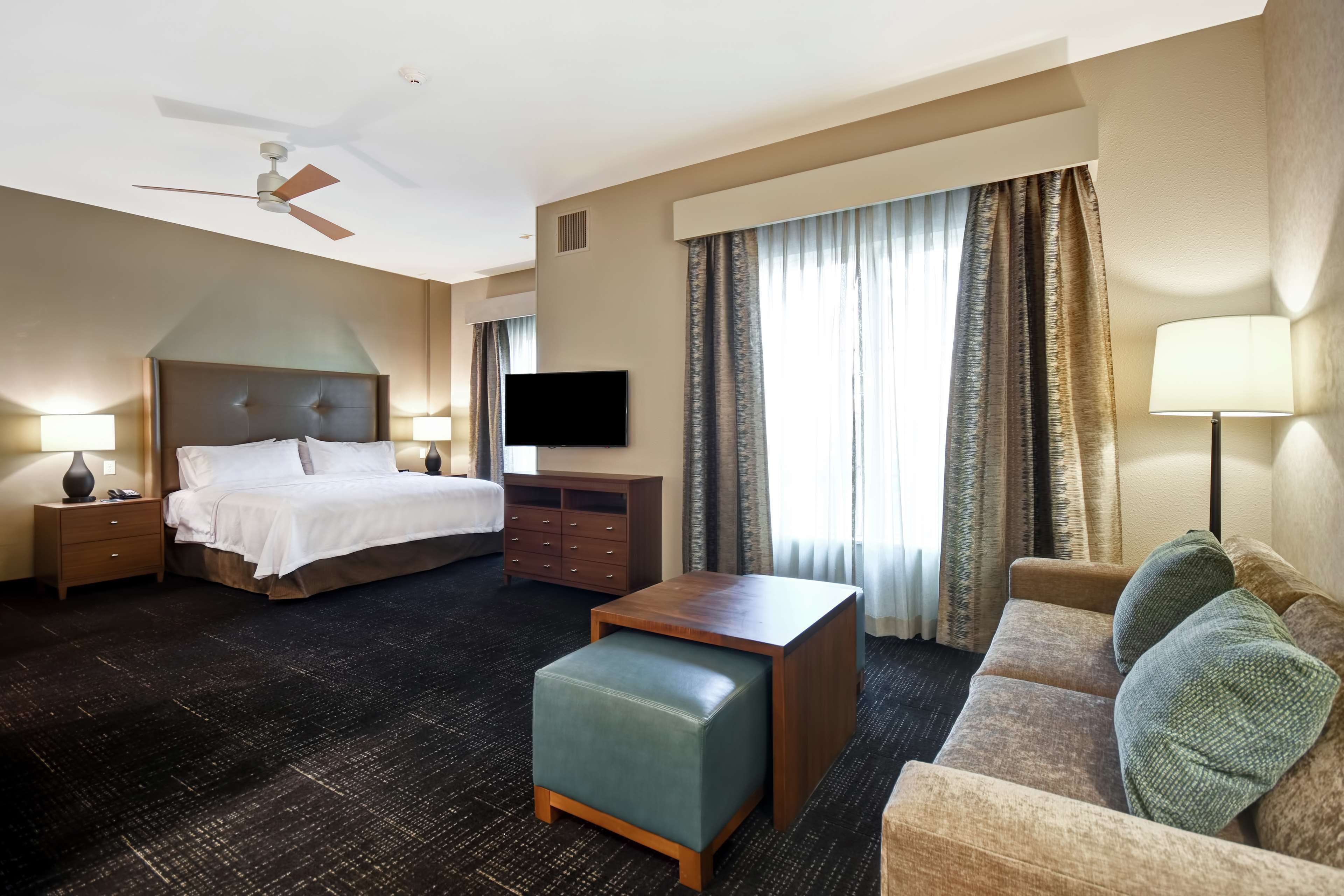 A hotel room with a bed, a sofa, a coffee table, a TV, and a ceiling fan.