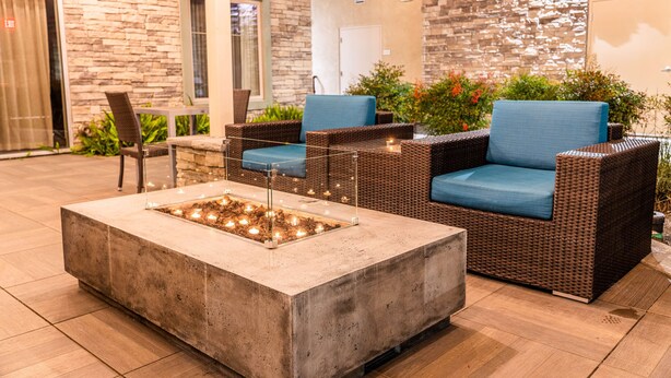 A patio area with wicker furniture, a concrete fire pit, and a stone wall backdrop.