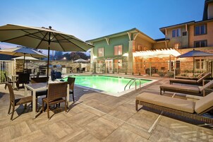 A pool area with lounge chairs and a table, surrounded by a stone wall and a building with a stone facade.