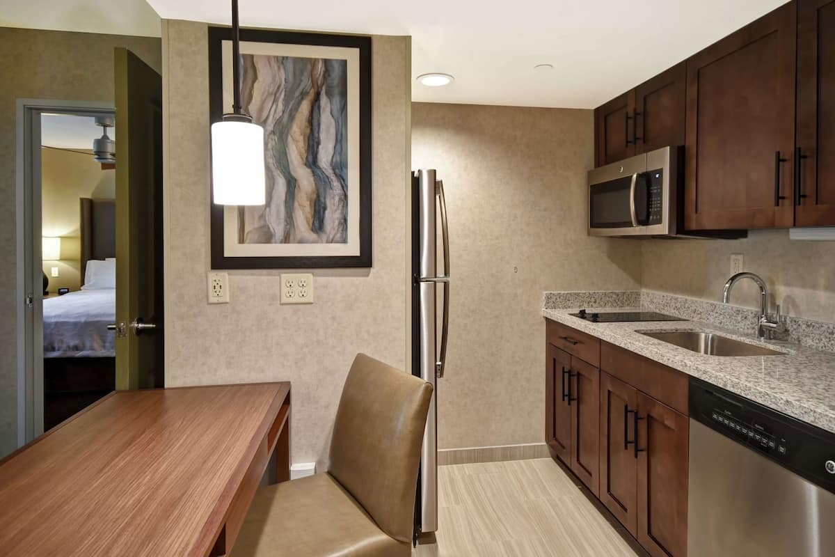 Habitación de hotel compacta con kitchenette, un comedor con mesa y silla de madera, refrigerador, microondas y un cuadro en la pared.