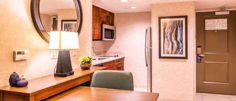 A hotel room with a wooden dining table, a microwave, a refrigerator, a sink, and a large mirror.