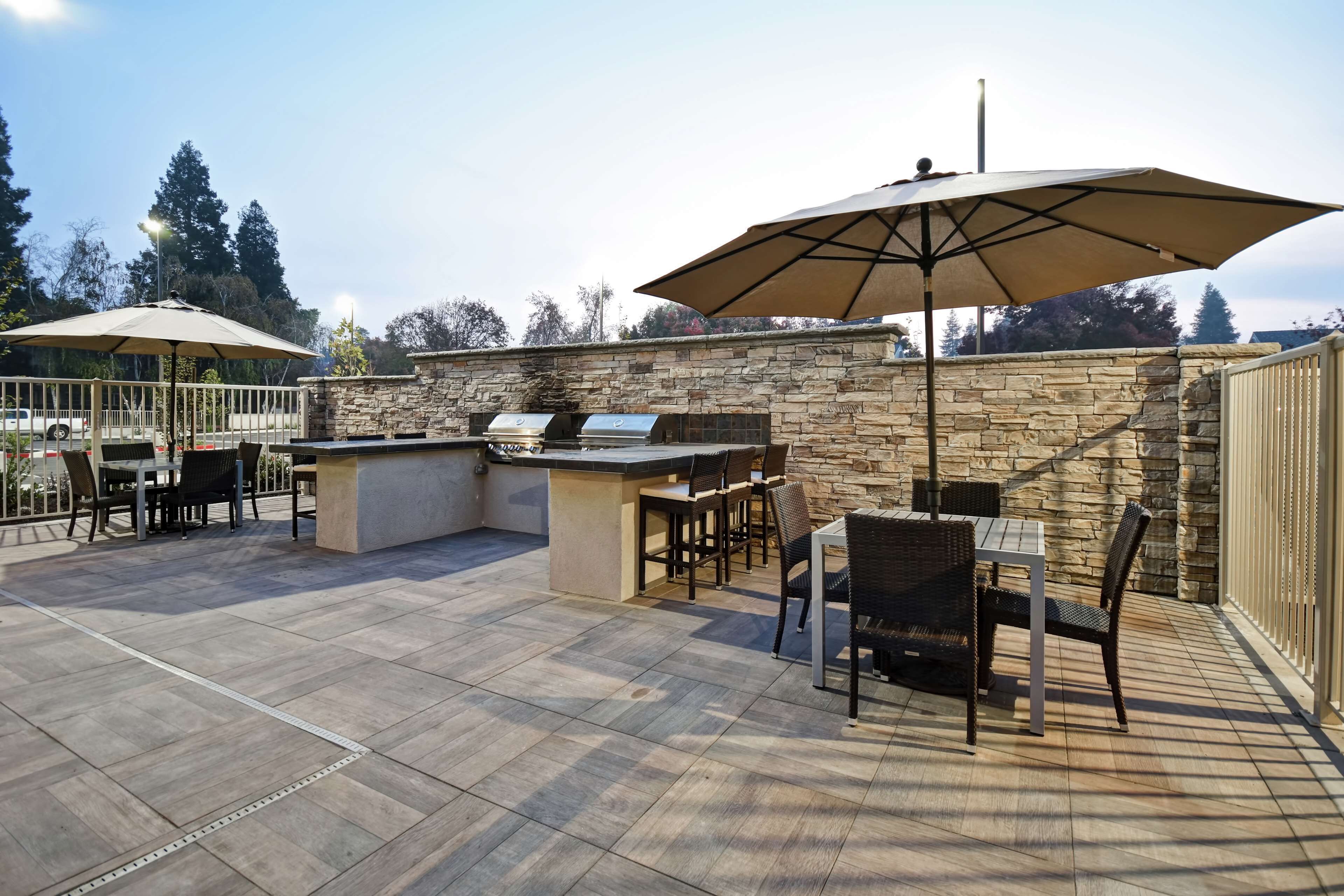 An outdoor patio with stone walls, a barbecue grill, and a table with chairs.