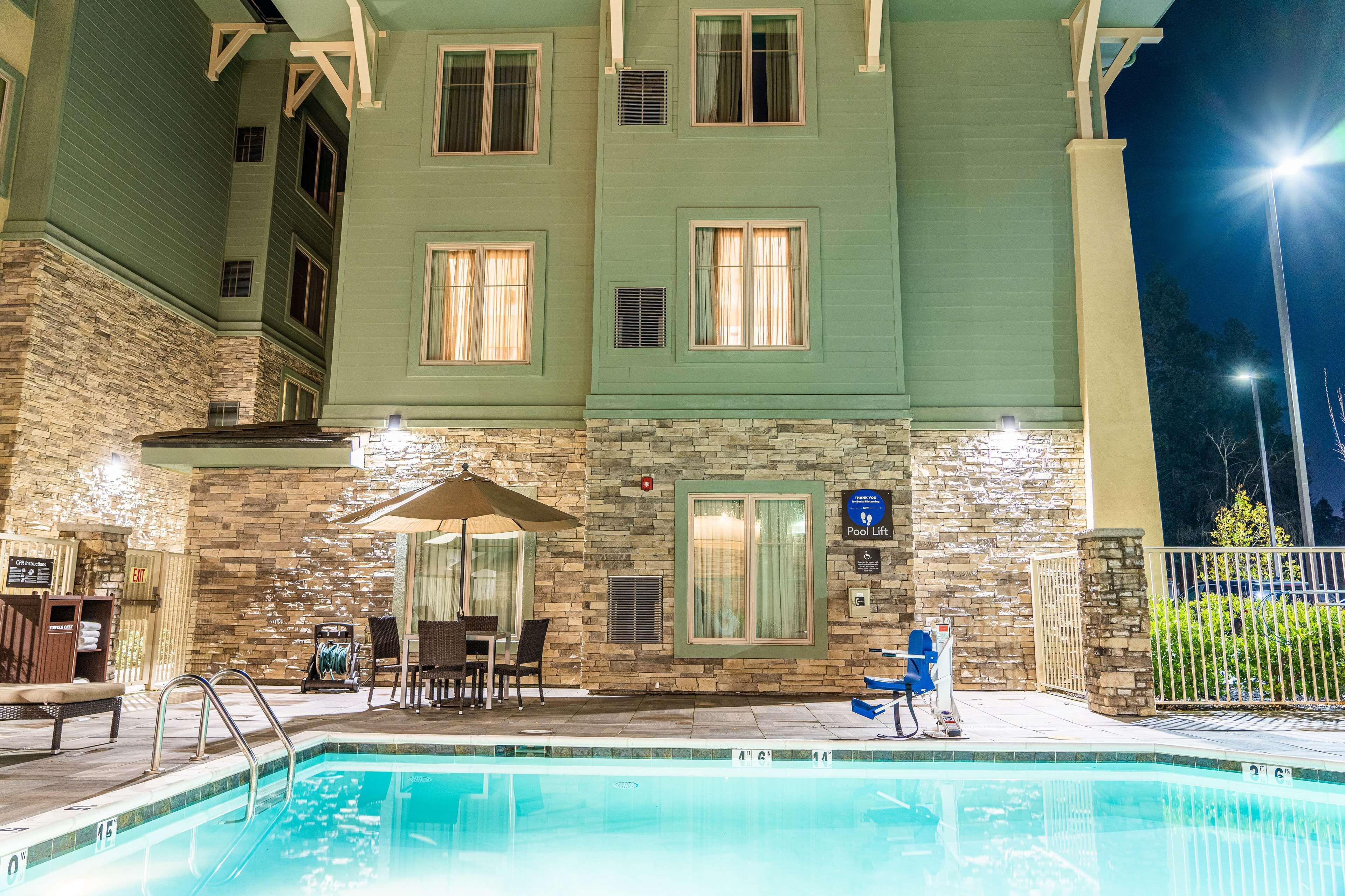A pool area with a stone wall, a pool lift, and a covered seating area with chairs and a table.