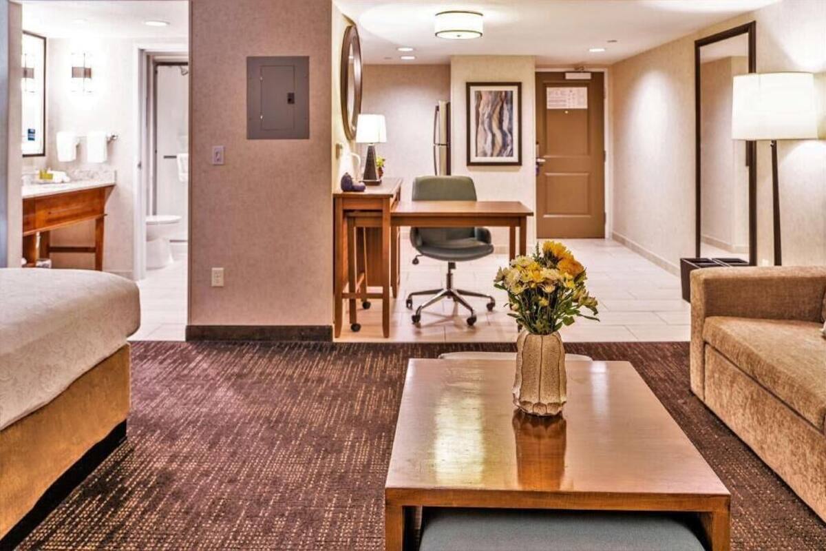 Een hotelkamer met een bed, een bureau met stoel, een bijzettafeltje met vaas en een bank.