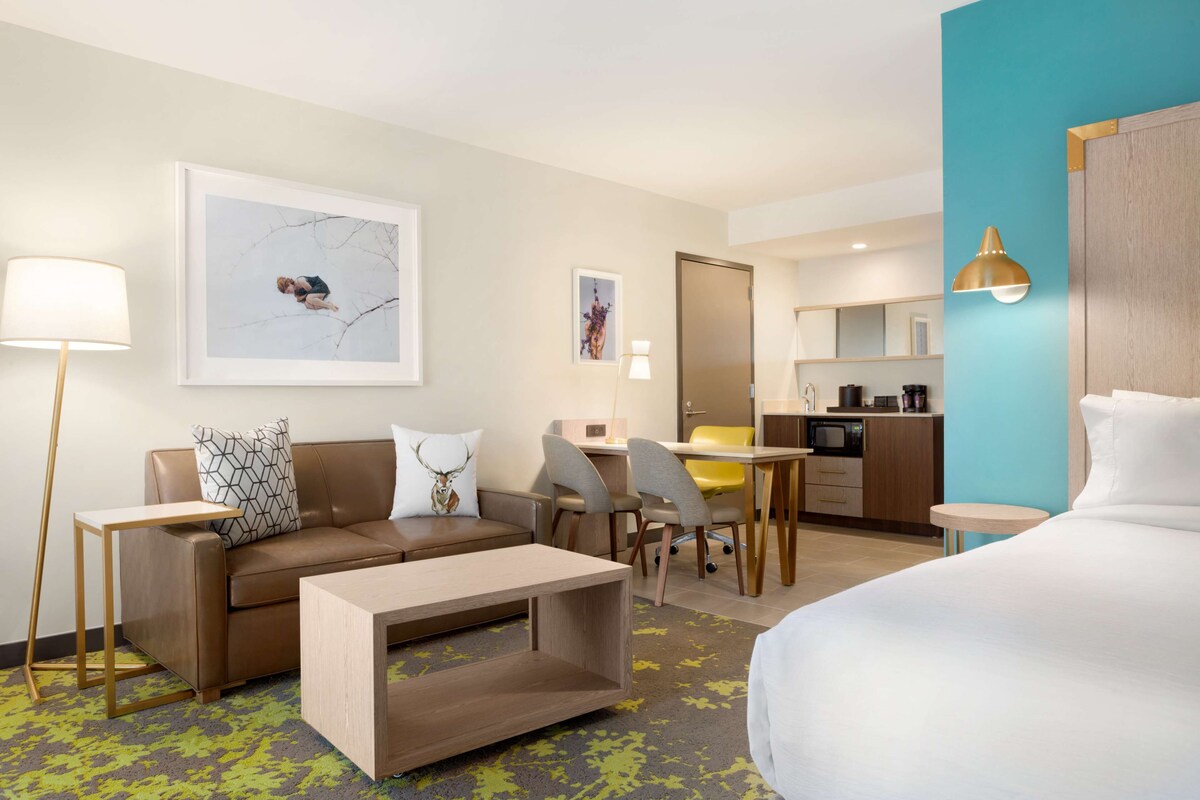 Una habitación de hotel con cama, sofá, mesa de centro, escritorio y kitchenette.