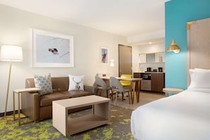 A hotel room with a bed, a sofa, a coffee table, a desk, and a kitchenette.