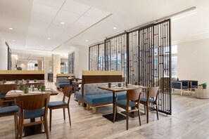 A modern restaurant with wooden tables and blue cushioned seating, a high ceiling, and a decorative partition with vertical lines. - Embassy Suites by Hilton Boulder (Boulder)