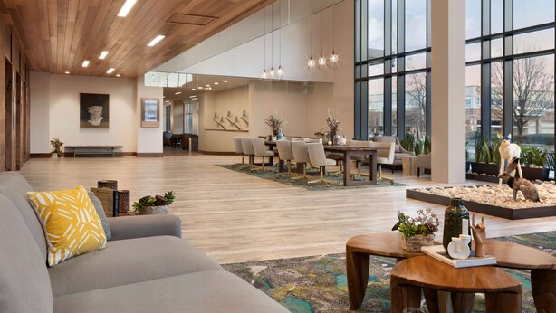 Un lobby espacioso con techo de madera, amplias ventanas, zona de estar y una escultura decorativa.
