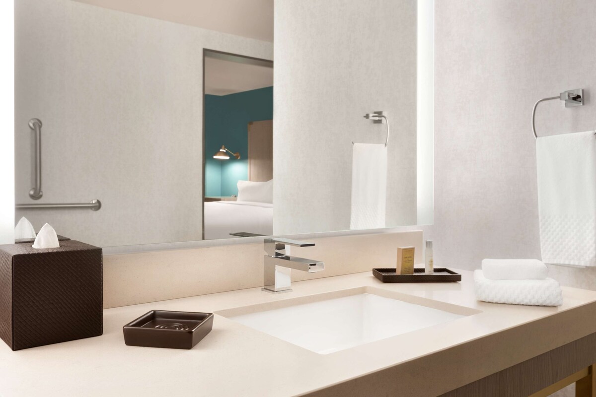 Un baño moderno con un espejo grande, un lavamanos, un perchero para toallas y una barandilla.