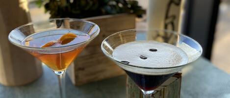 Dos copas de martini sobre una mesa texturizada, con un bloque de madera y una planta de fondo.