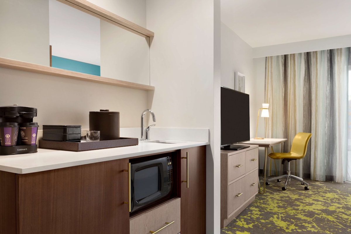 Habitación de hotel compacta con kitchenette, televisión de pantalla plana, escritorio y una silla.