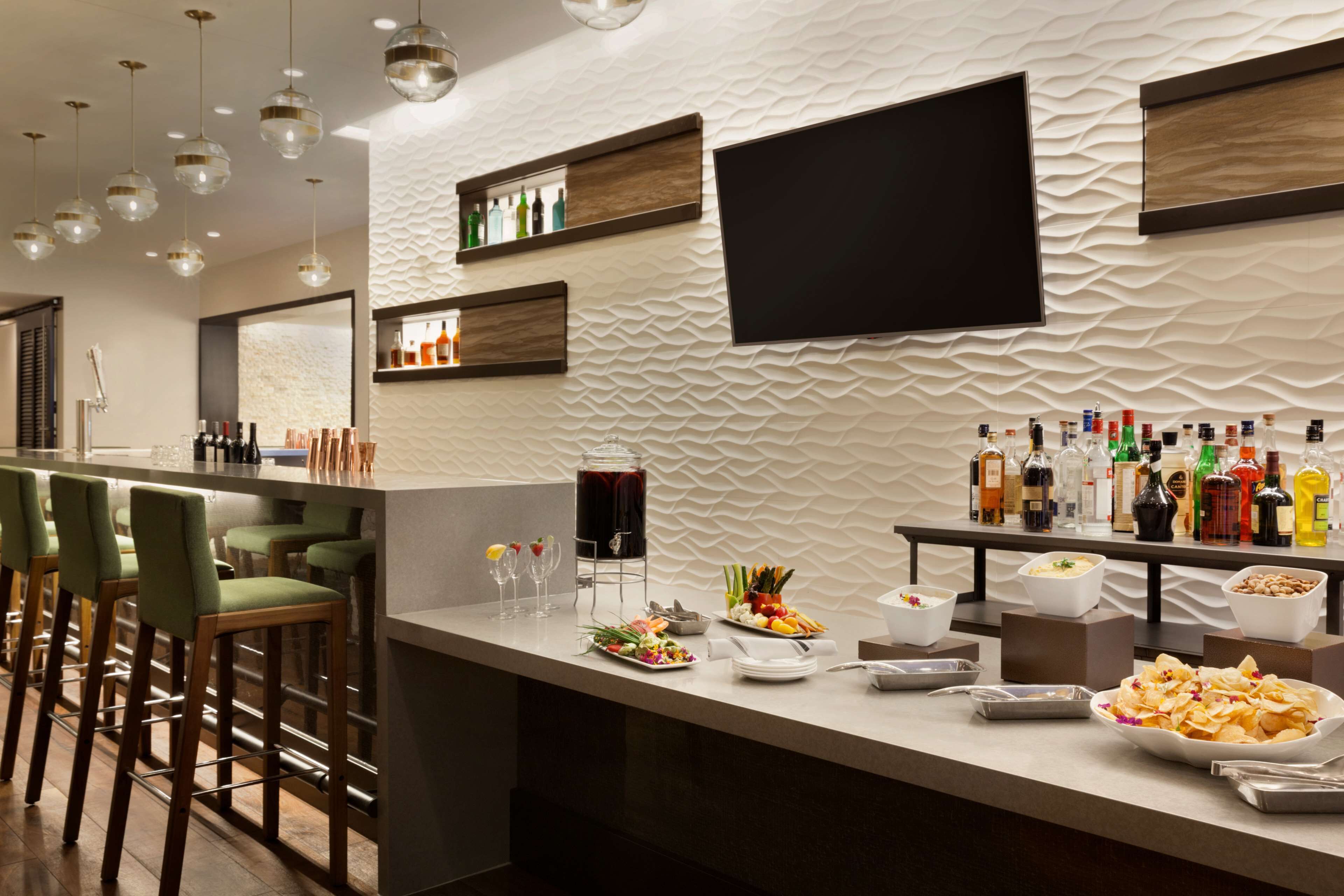 A modern bar area with a long counter, bar stools, and a variety of food and drink options.