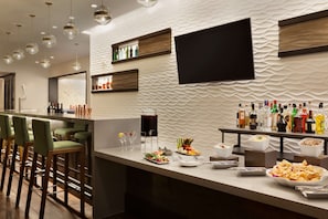 A modern bar area with a long counter, bar stools, and a variety of food and drink options.