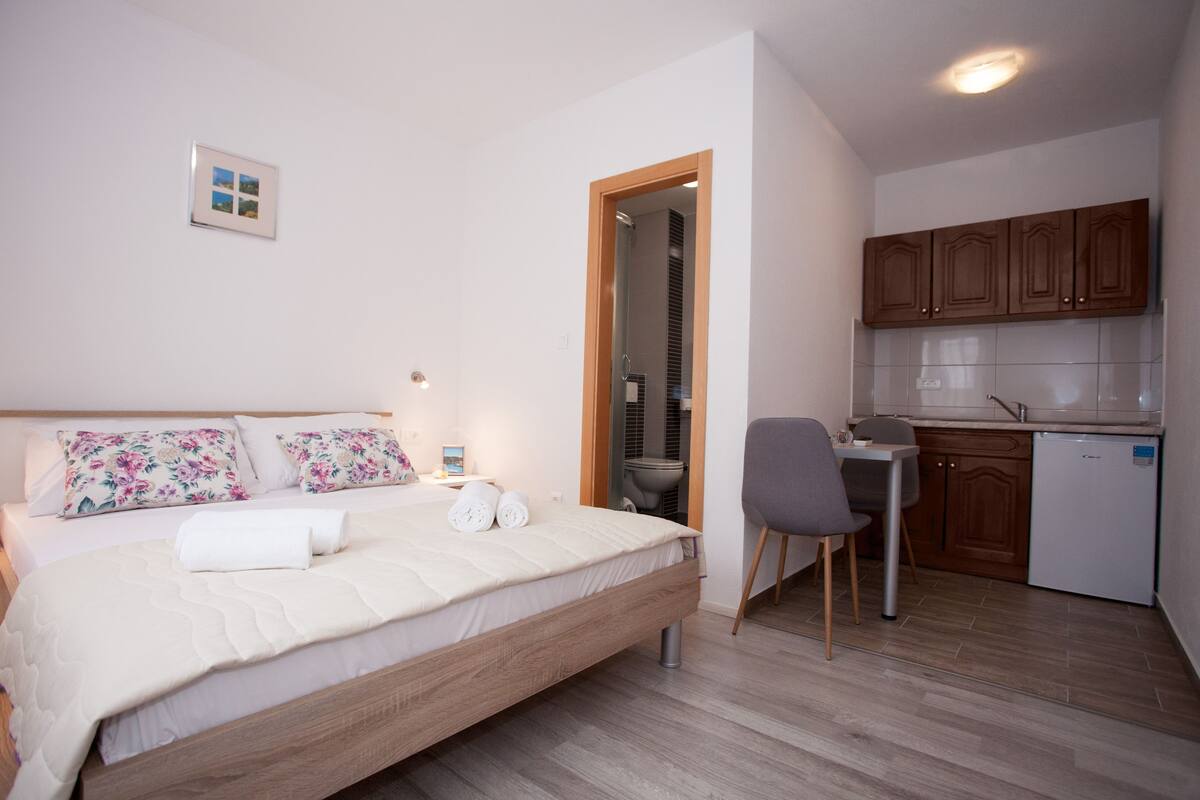 A bedroom with a bed, a desk, and a kitchenette.