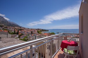 A balcony with a table and chair, overlooking a coastal town and the sea. - Villa MIA (Baska Voda)