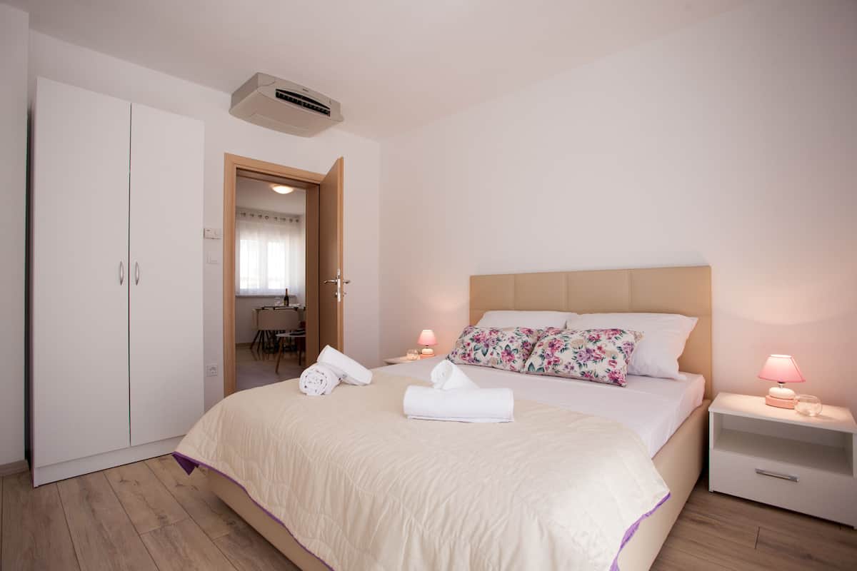 A bedroom with a bed, nightstands, a wardrobe, and an air conditioning unit.