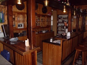 Una zona de bar con barra, taburetes y estantes llenos de botellas y vasos.