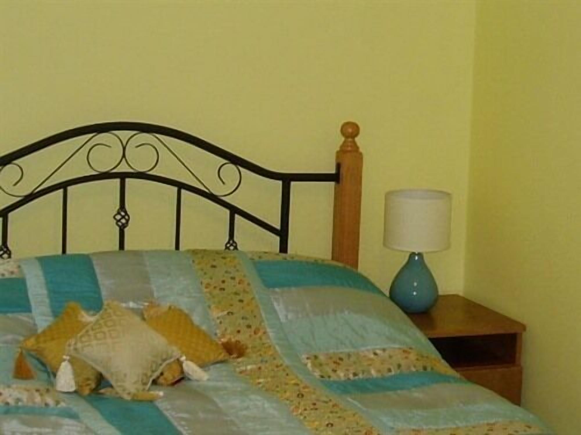Una cama con colcha a rayas, cabecera de madera, lámpara de noche y mesita.