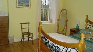 A bedroom with a wooden bed, a chair, a dresser, a window with a view, and a mirror. - The Gardener's Cottage (Kilvarnet)