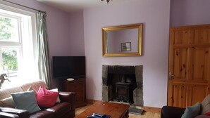 A living room with a fireplace, a television, a sofa, and a wooden coffee table. - The Gardener's Cottage (Kilvarnet)