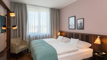 Ein Hotelzimmer mit einem großen Bett, einem Sessel, einem Fernseher und einem Nachttisch mit Lampe.