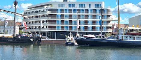 A waterfront building with multiple balconies, a dock with boats, and a clear sky.