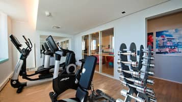 A gym with cardio machines, weightlifting equipment, and a dining area visible through glass doors.