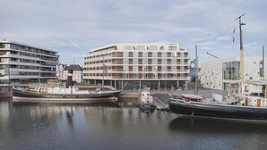 A marina with boats docked, a modern building labeled 'The Liberty,' and a flagpole with a flag. - THE LIBERTY Hotel Bremerhaven, BW Signature Collection (Bremerhaven)