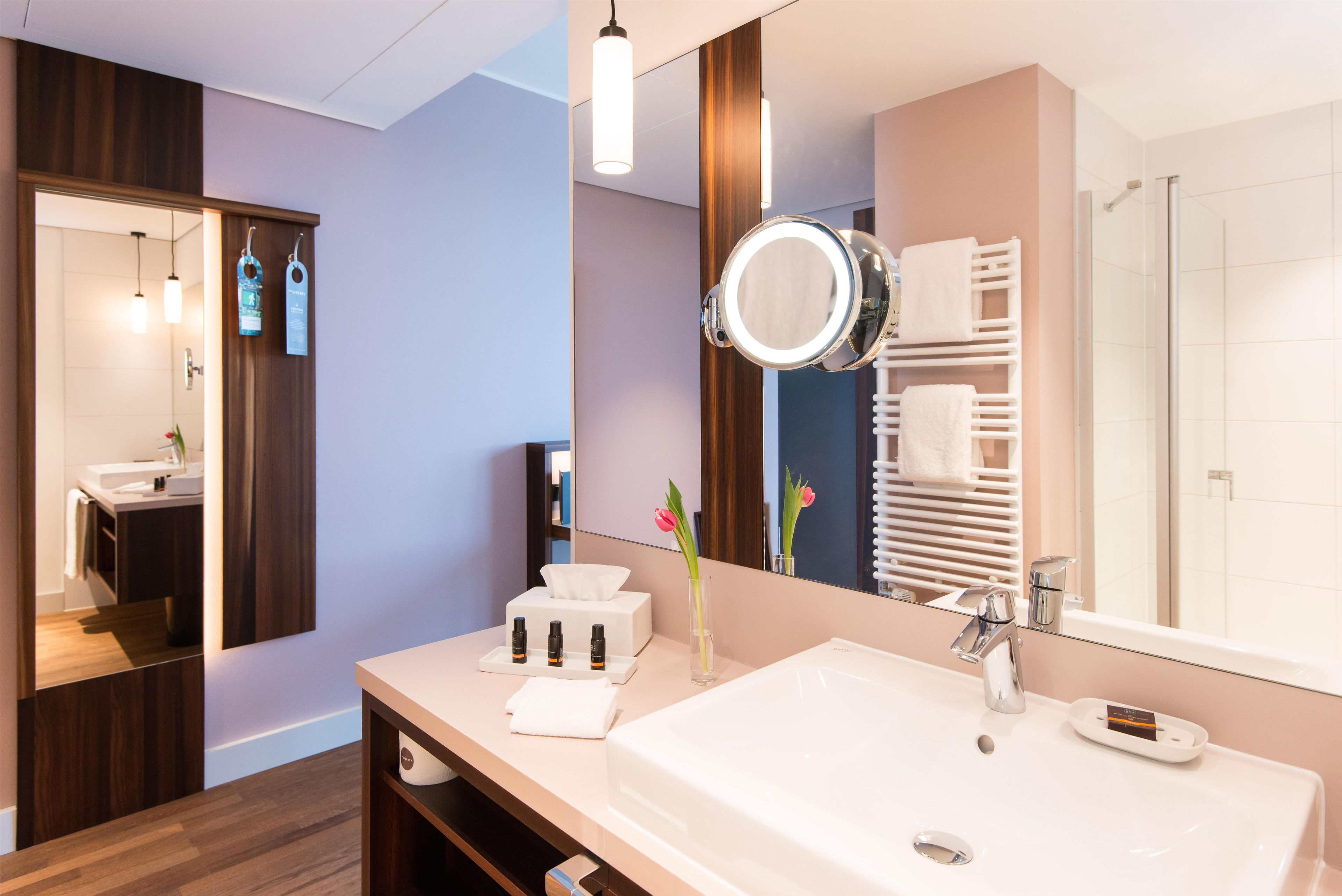 A modern bathroom with a large mirror, a sink, and a towel rack.