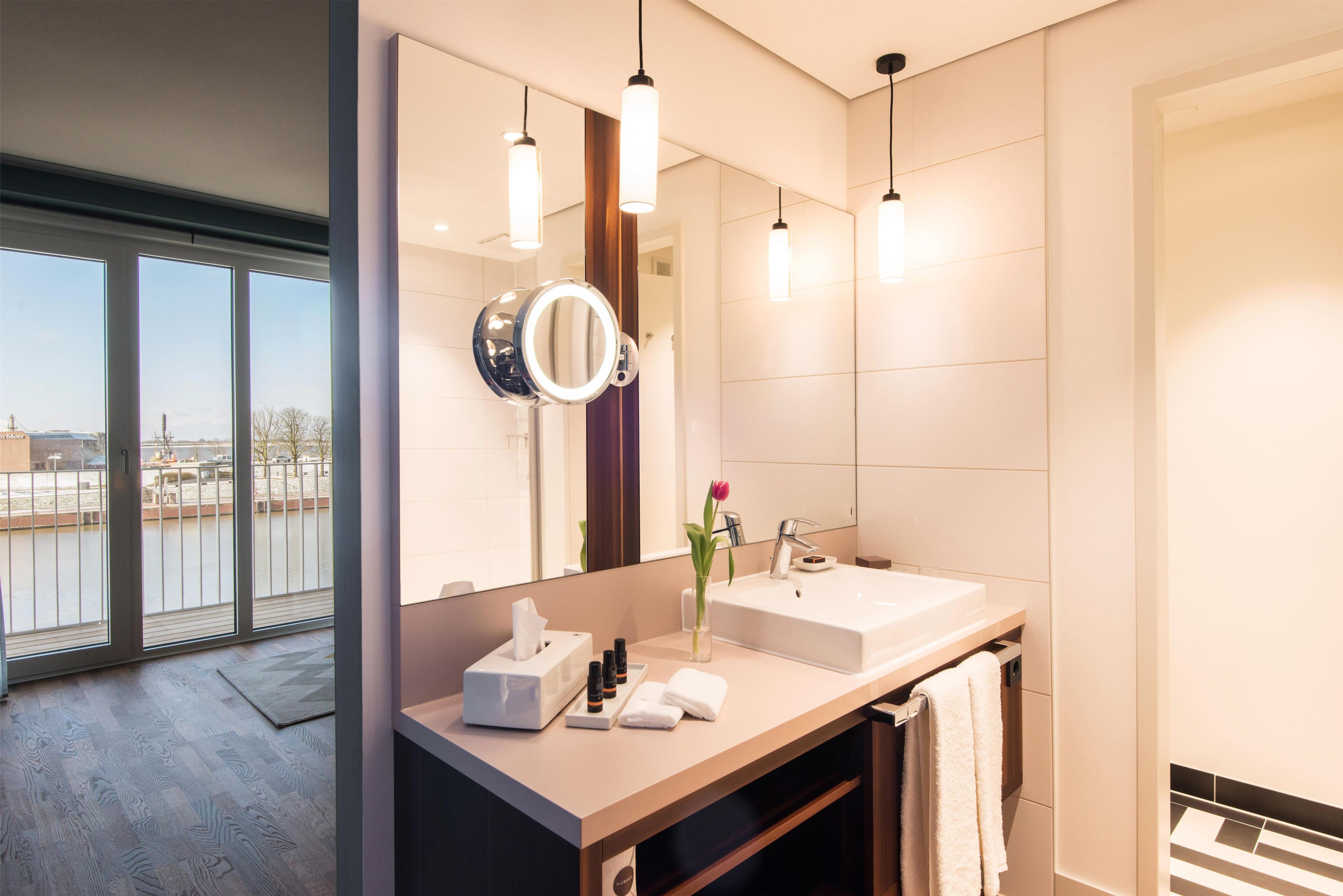 A modern bathroom with a large mirror, two sinks, and a view of a building through the window.