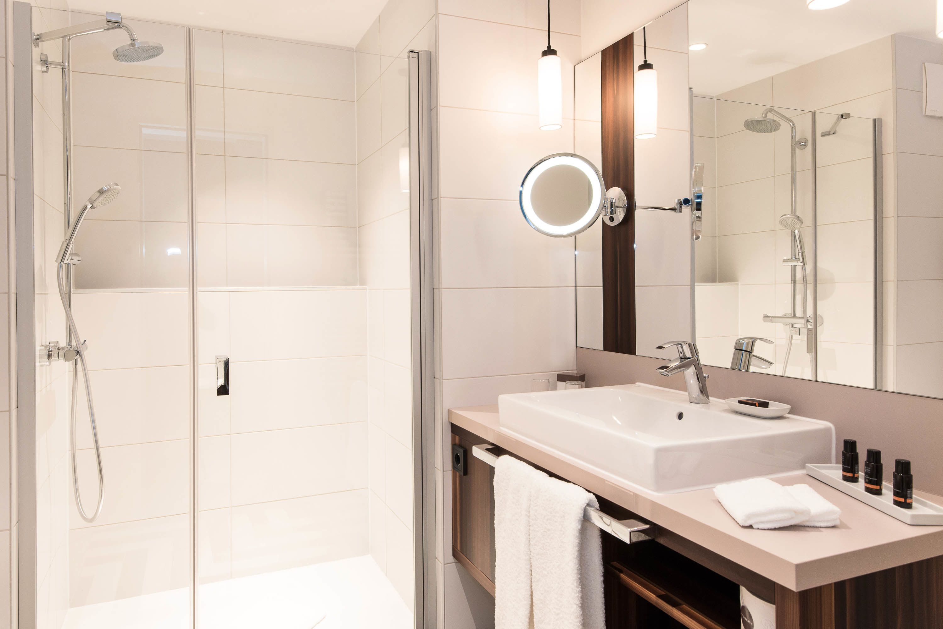 Un baño moderno con ducha envuelta en vidrio, un espejo grande y un tocador con lavabo y artículos de aseo.