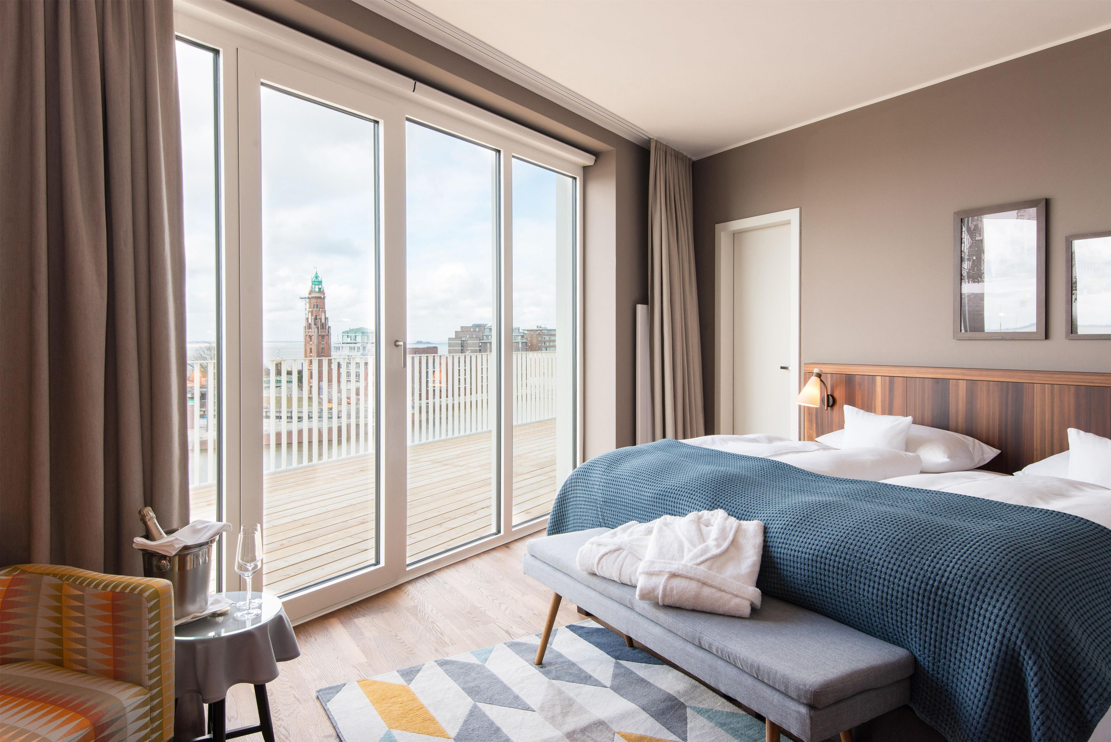 Een hotelkamer met een groot bed, een bank, een klein tafeltje met een fles en een glas, en een stadsgezicht door ramen van de vloer tot aan het plafond.