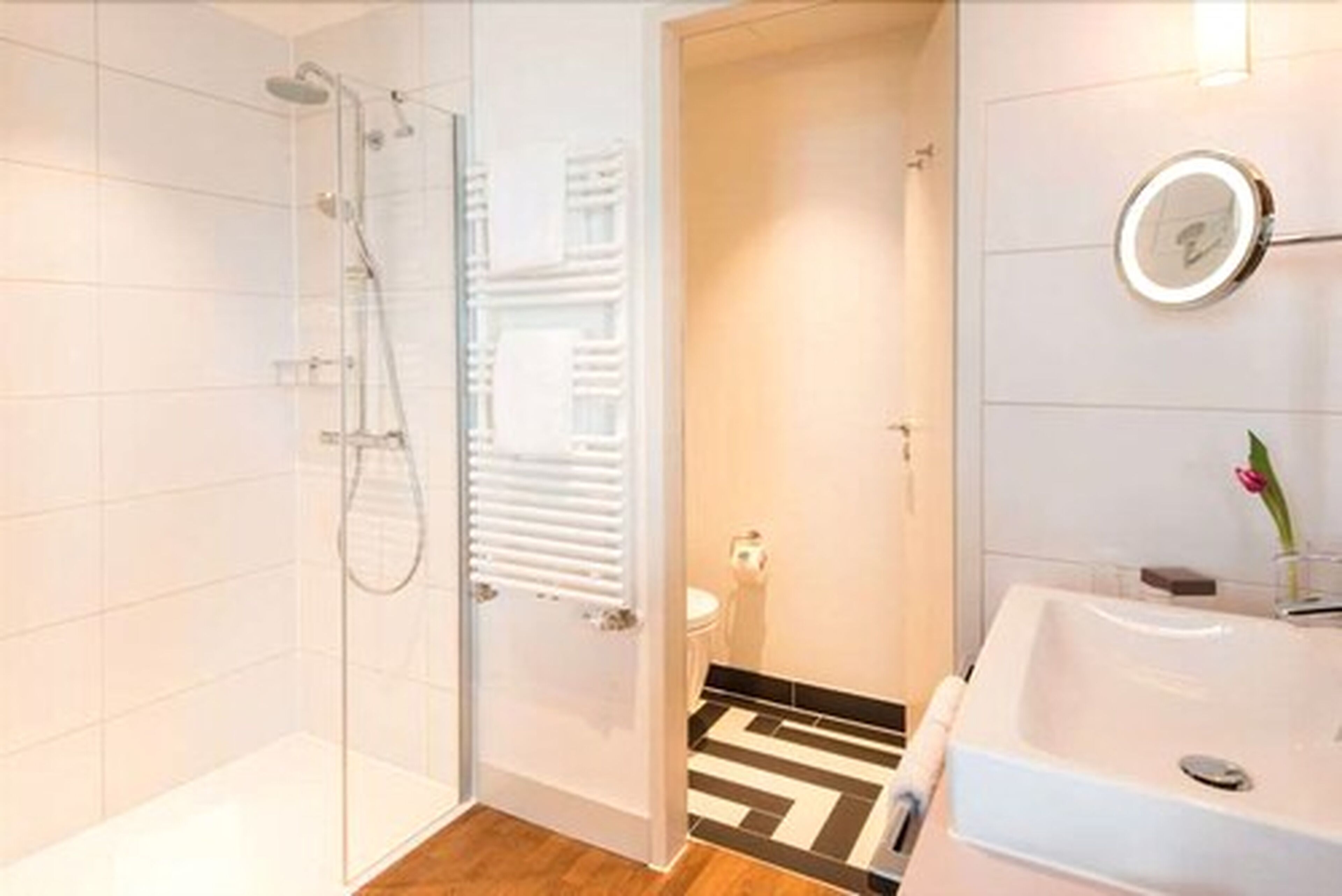 A modern bathroom with a glass shower enclosure, a white sink, and a mirror with a light.