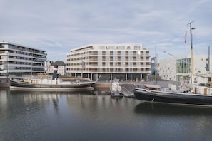 Un puerto deportivo con barcos amarrados, un edificio moderno con el rótulo 'The Liberty' y un asta con una bandera.